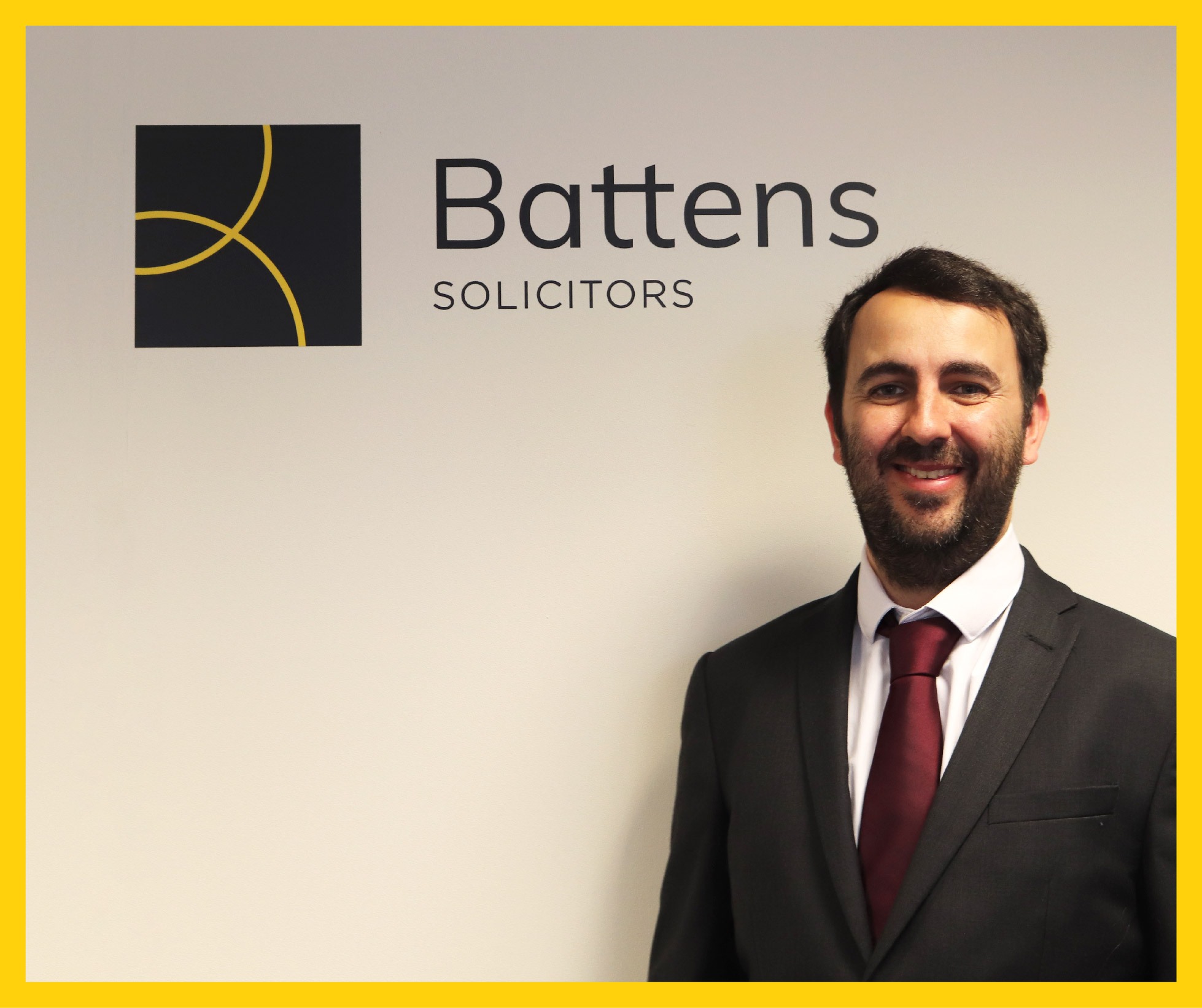 A senior associate solicitor stood in front of a white wall with the Battens Solicitors logo